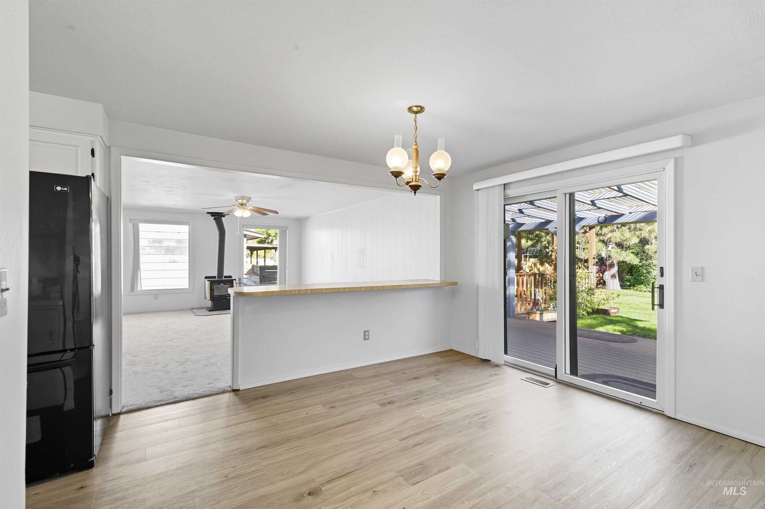 Unfurnished dining area featuring a wood stove, light wood-type flooring, a chandelier, and a ceiling fan