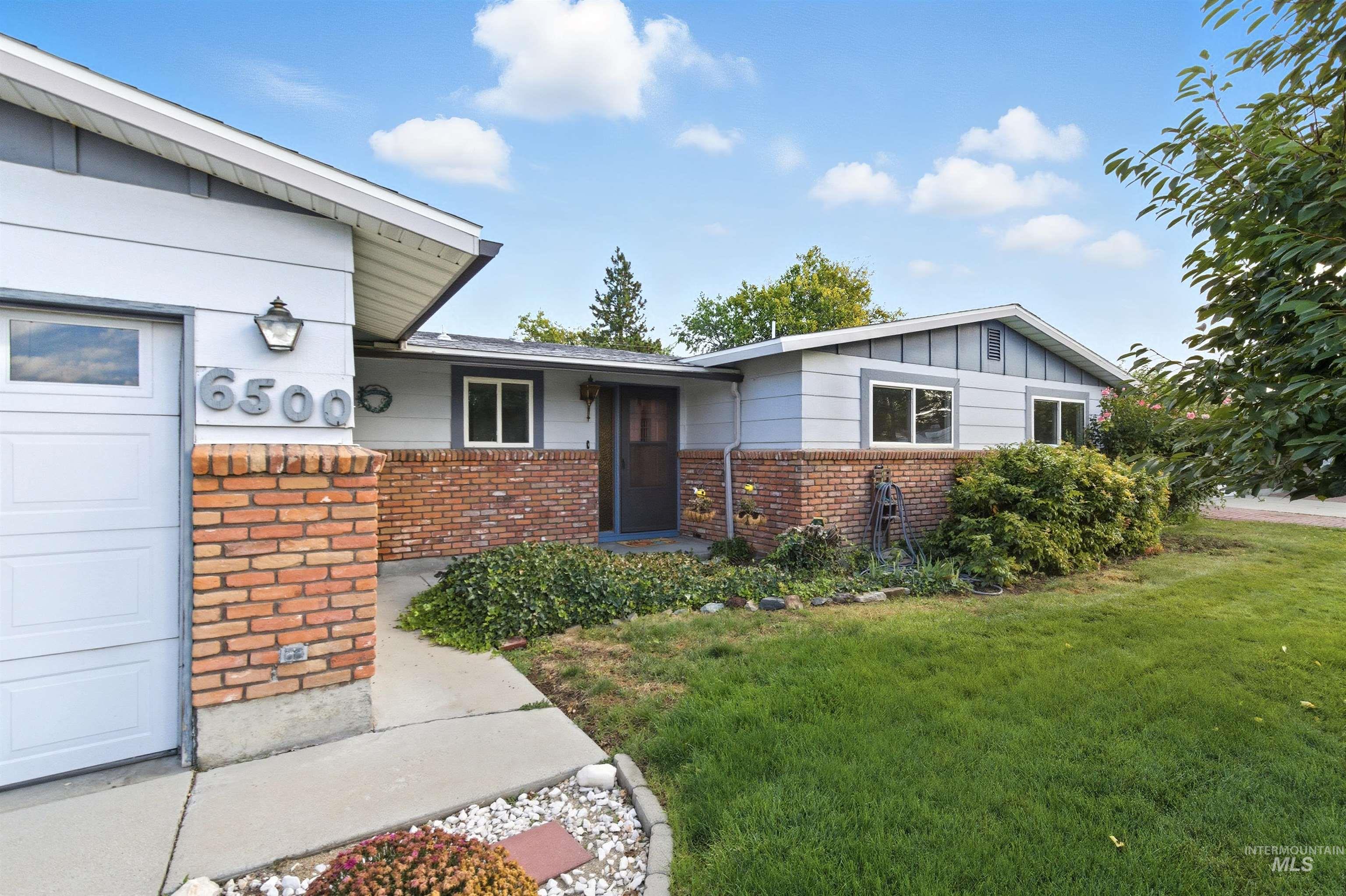 View of front facade featuring a front yard, brick siding, board and batten siding, and a garage