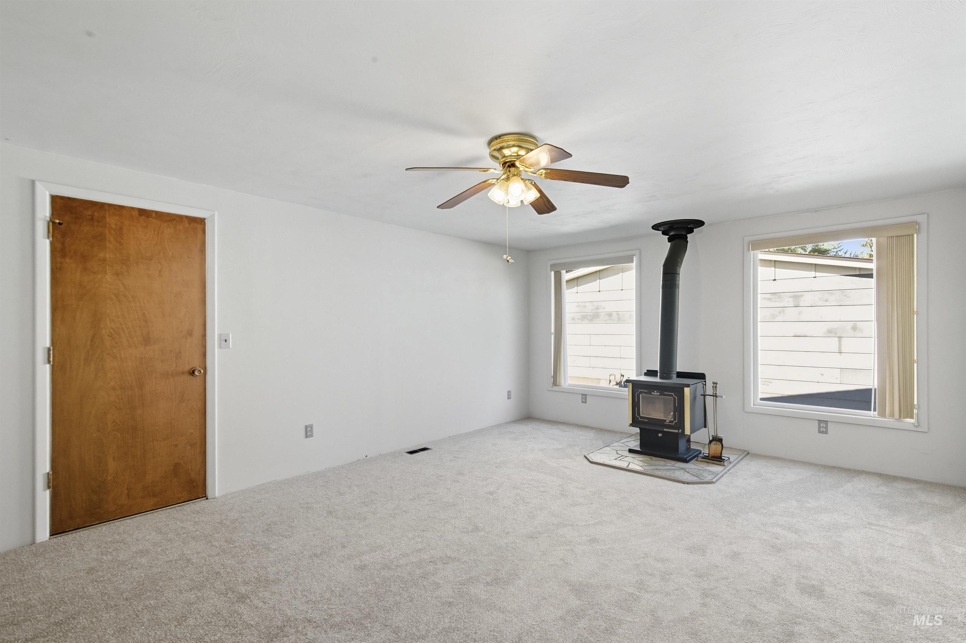Unfurnished living room with a wood stove, carpet, and a ceiling fan