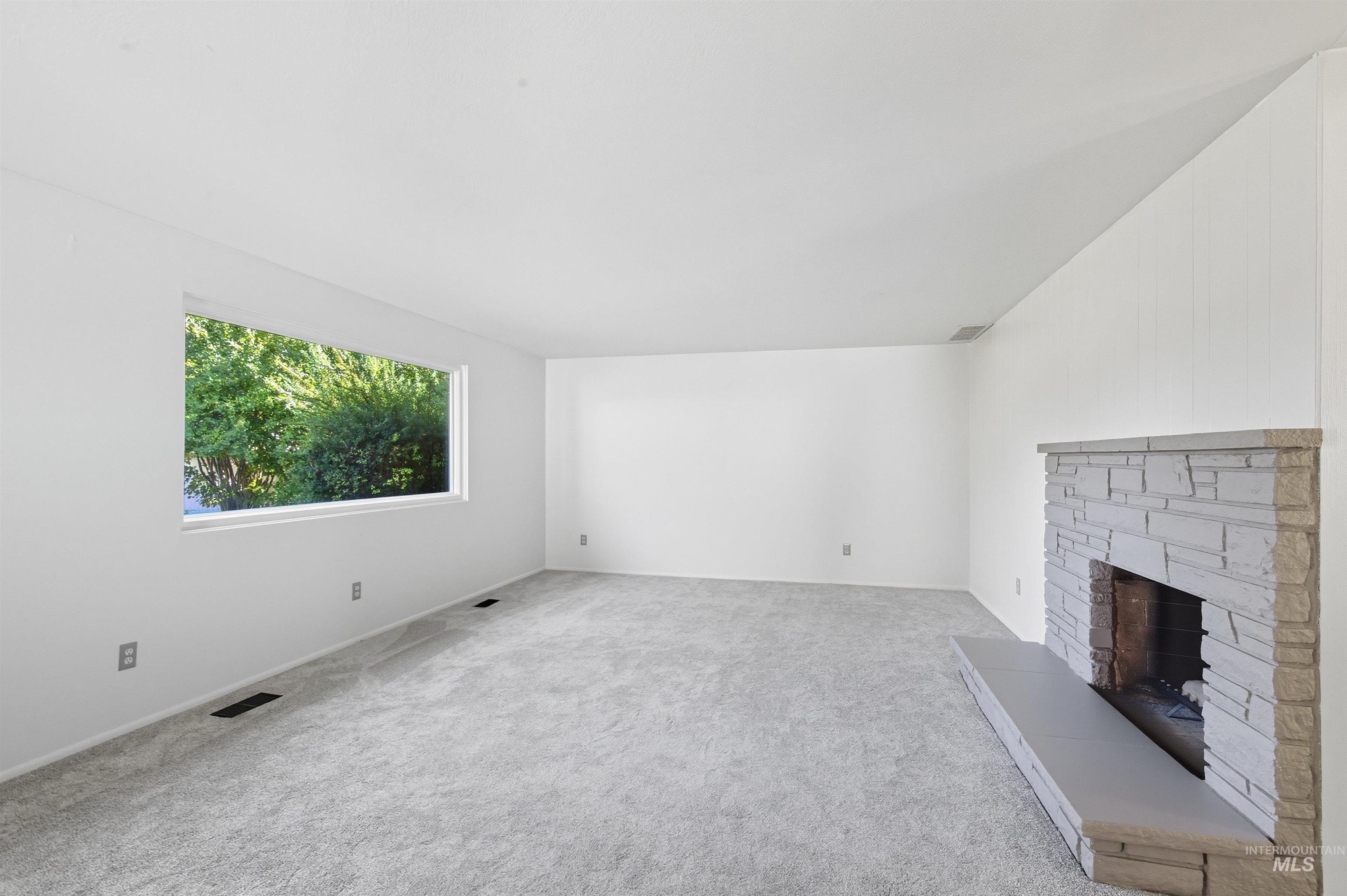 Unfurnished living room with a fireplace with raised hearth and light carpet