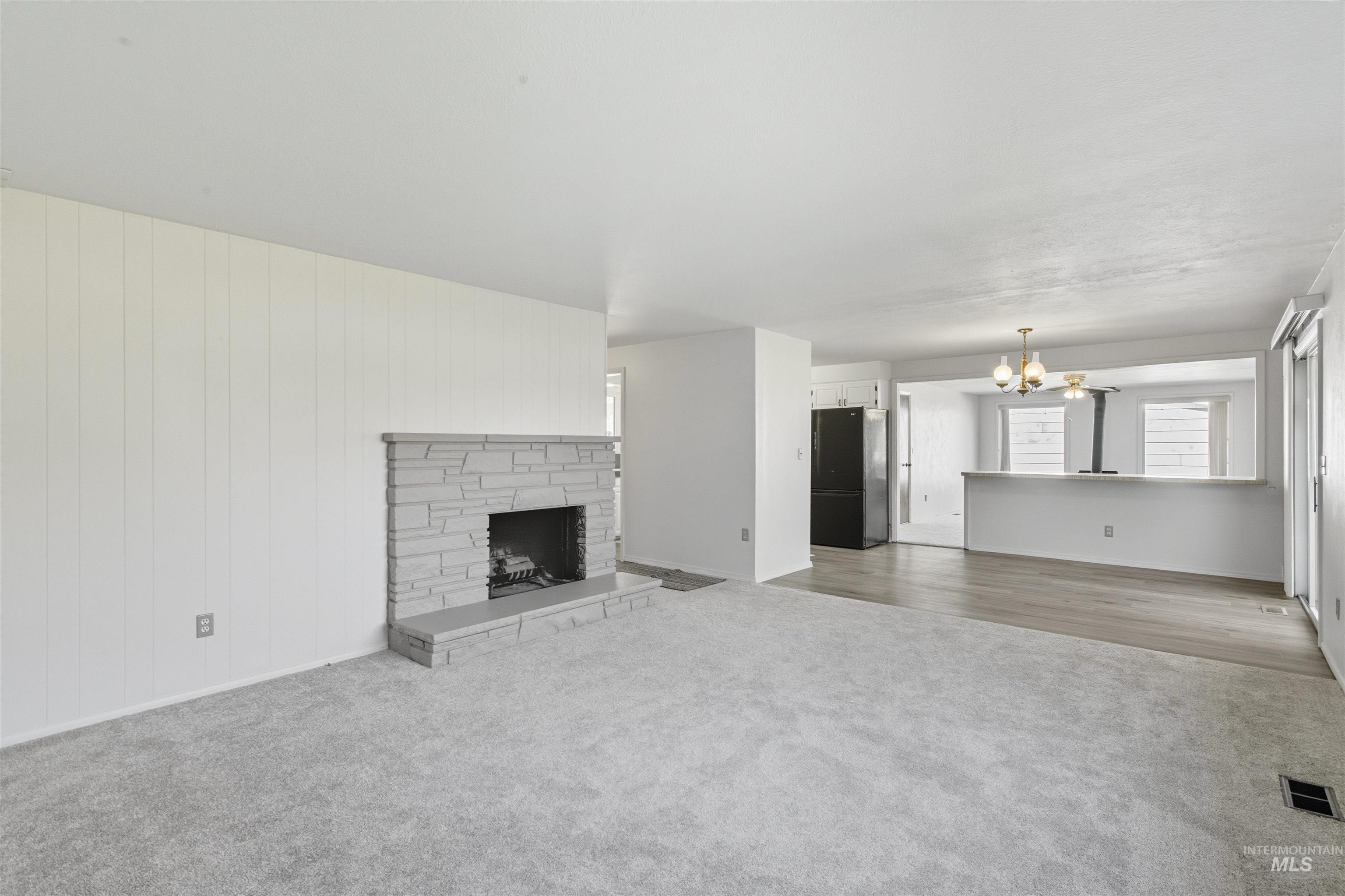 Unfurnished living room featuring a fireplace with raised hearth, carpet, and a chandelier