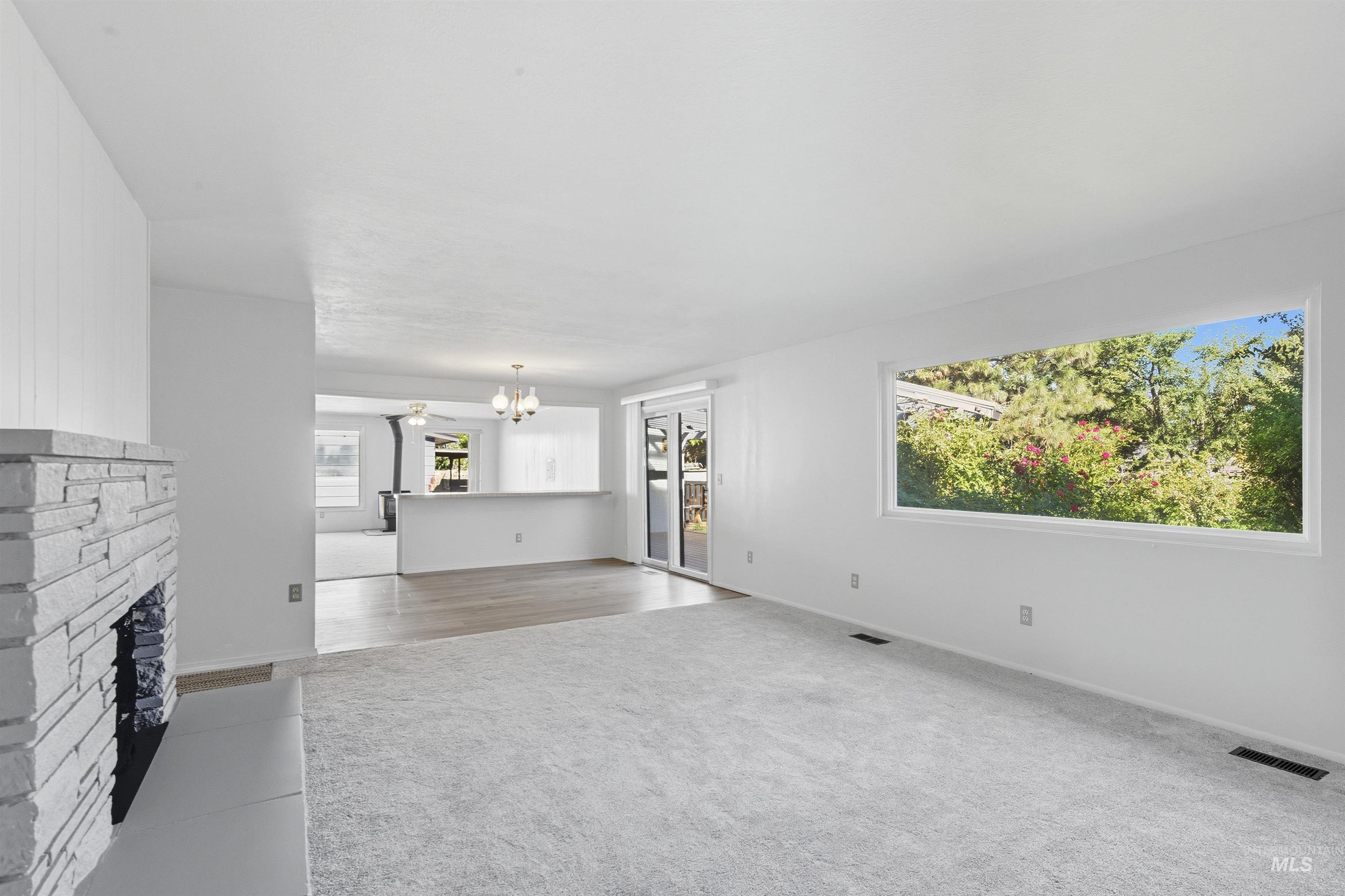 Unfurnished living room with light colored carpet, a stone fireplace, and a chandelier