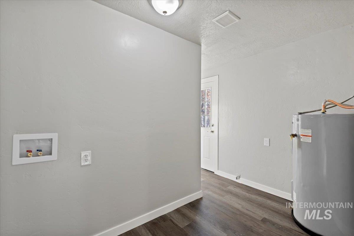 Washroom with electric water heater, hookup for a washing machine, a textured ceiling, and dark wood-style floors