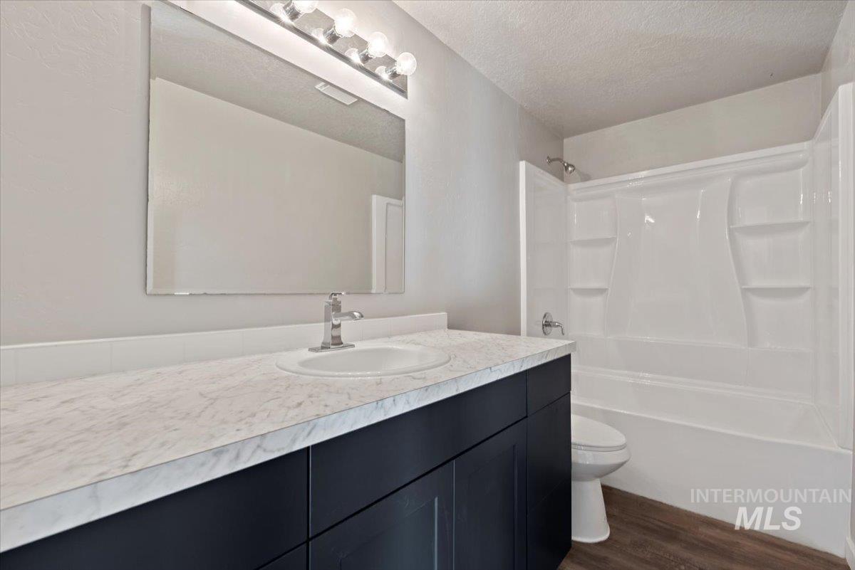 Full bath featuring vanity, a textured ceiling, shower / tub combination, and dark wood-type flooring
