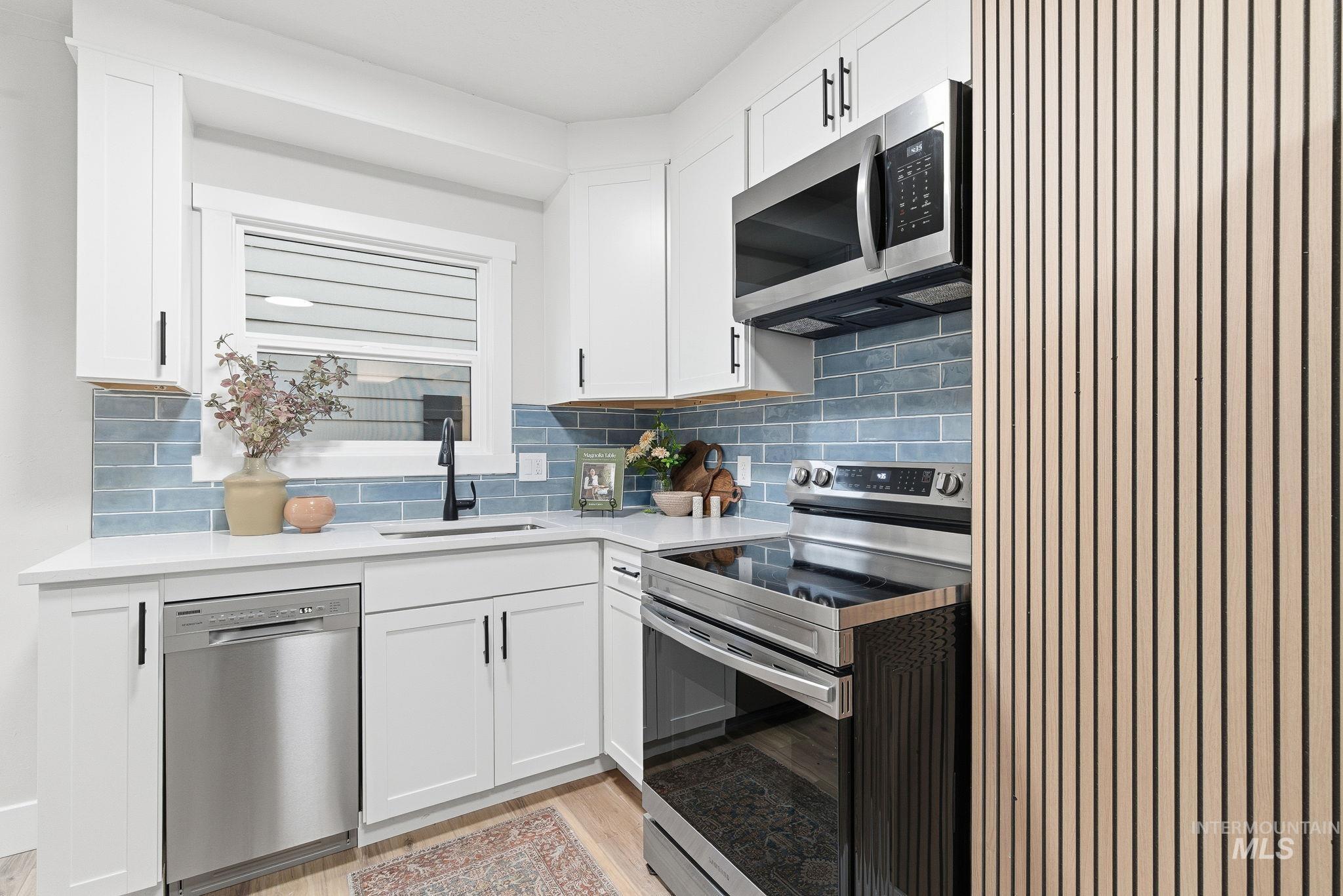 Kitchen featuring appliances with stainless steel finishes, white cabinets, and backsplash