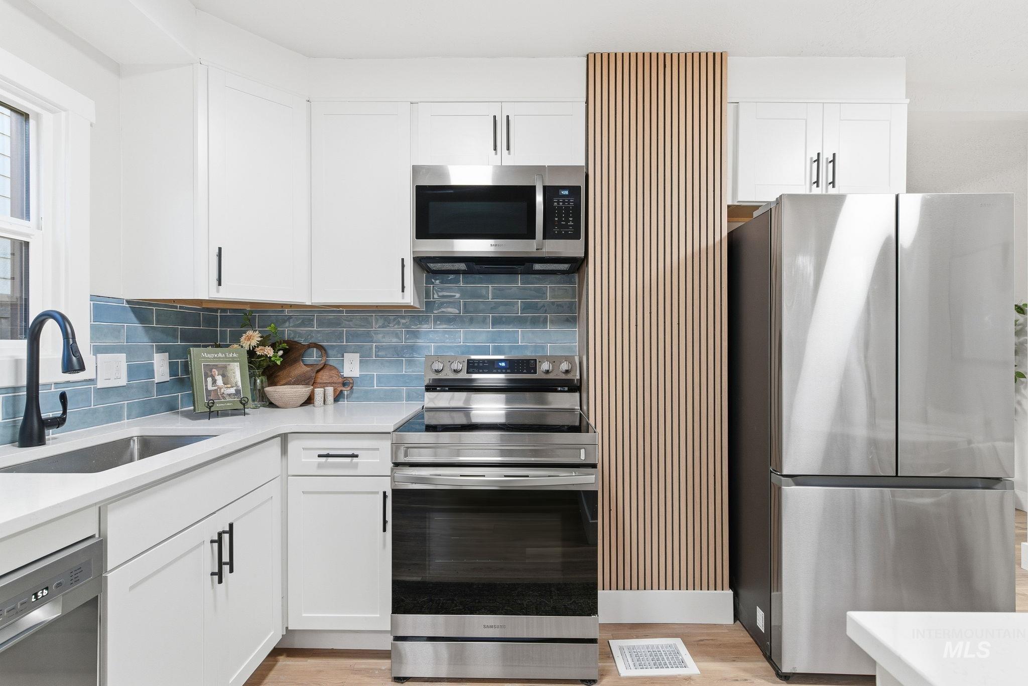 Kitchen featuring stainless steel appliances, white cabinets, backsplash, light stone countertops, and light wood-style flooring