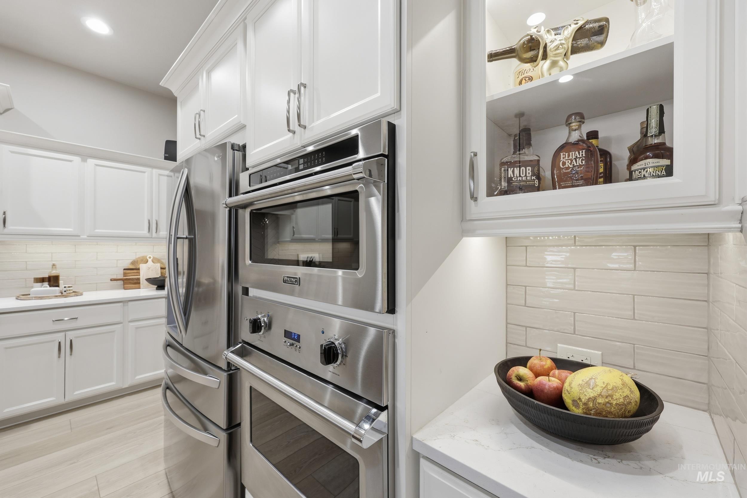 Kitchen featuring tasteful backsplash, white cabinets, stainless steel appliances, light stone counters, and recessed lighting