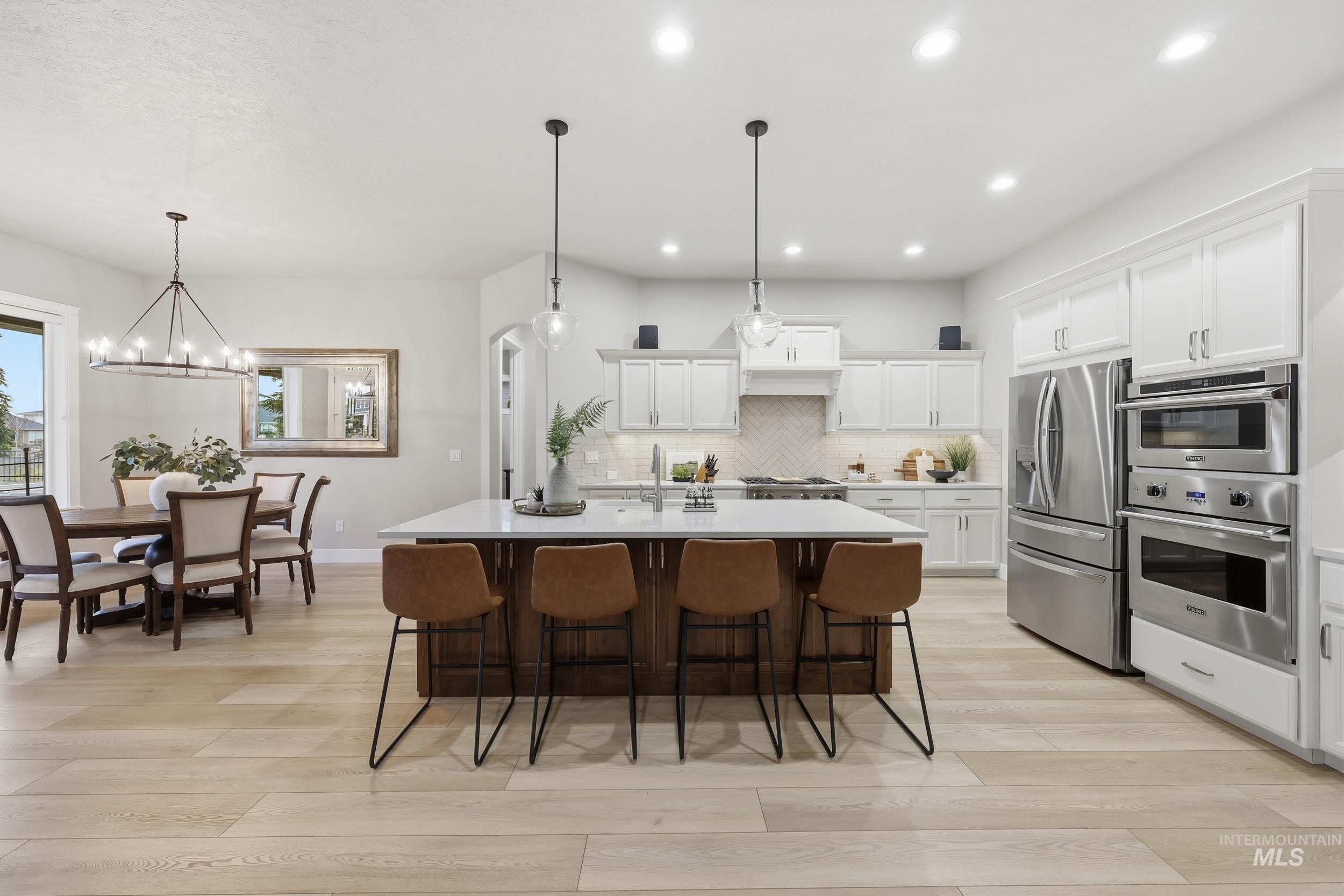 Kitchen with white cabinetry, appliances with stainless steel finishes, pendant lighting, an island with sink, and light wood-type flooring