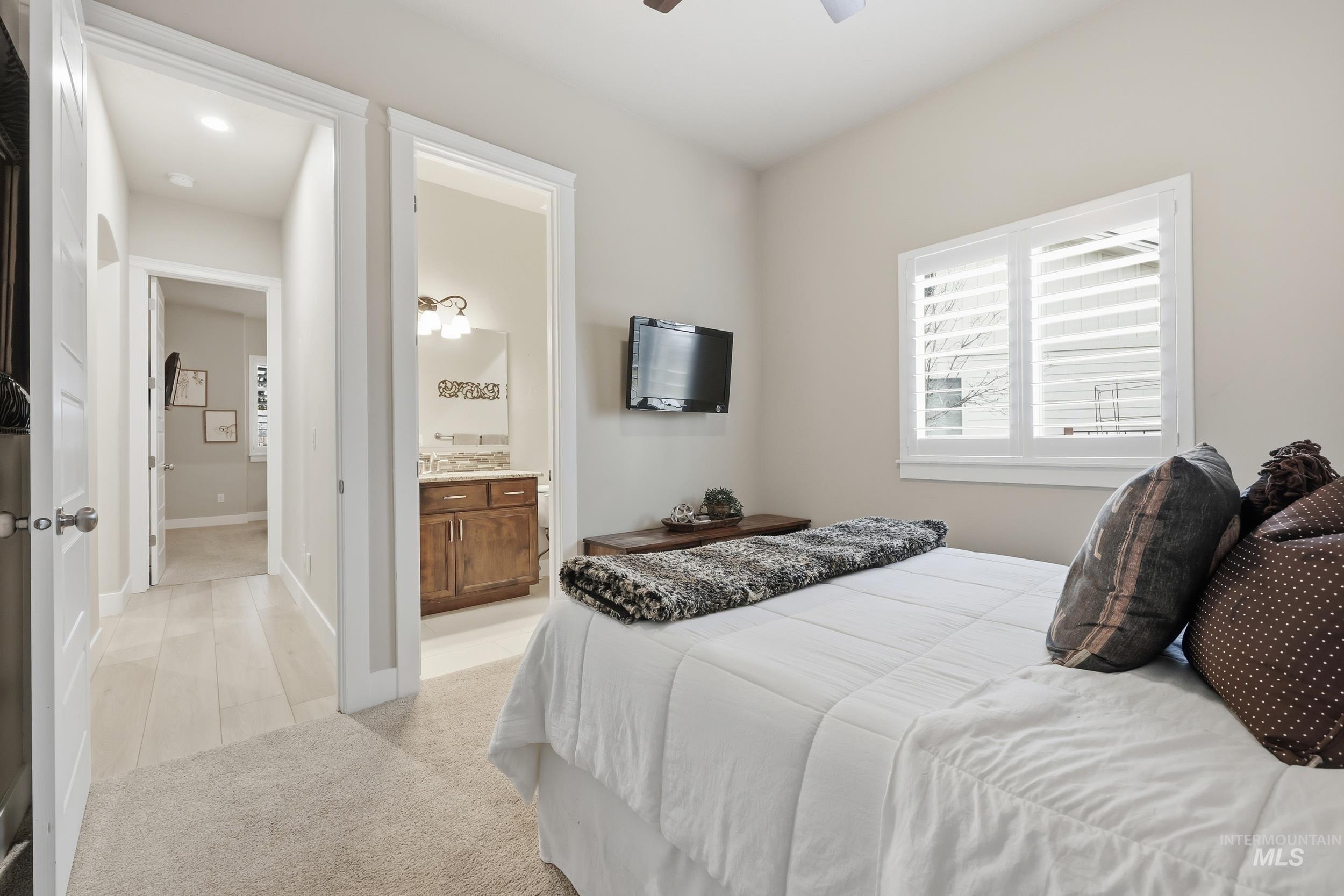 Bedroom with light carpet, ensuite bathroom, and ceiling fan