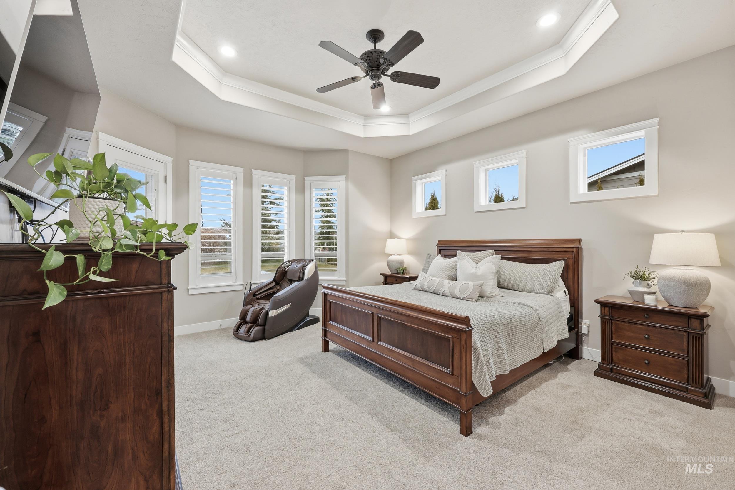 Bedroom featuring a ceiling fan, light colored carpet, multiple windows, crown molding, and a tray ceiling