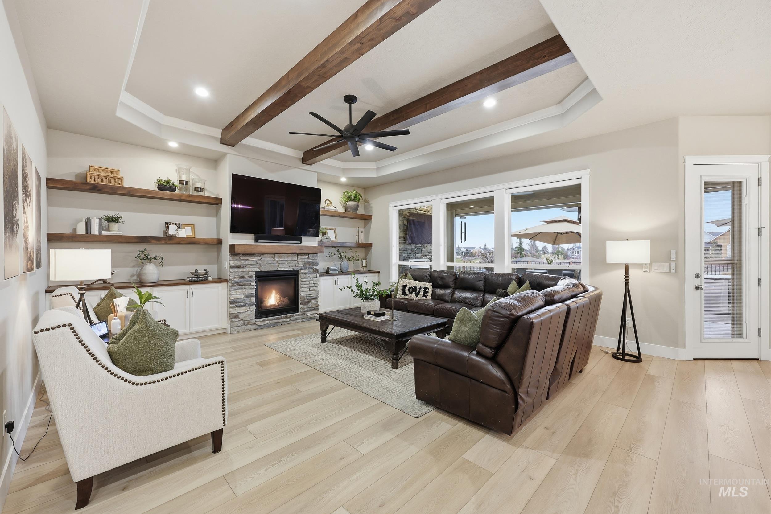 Living area with light wood-style flooring, beamed ceiling, ceiling fan, a stone fireplace, and recessed lighting