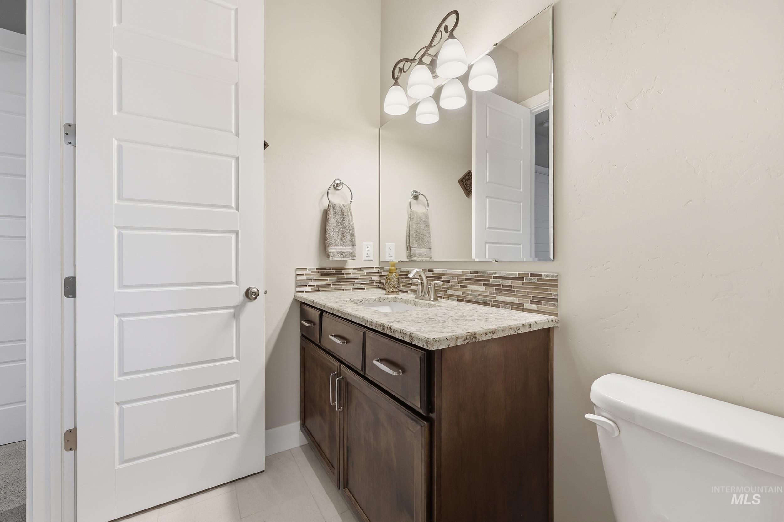 Half bathroom with decorative backsplash, vanity, and light tile patterned flooring