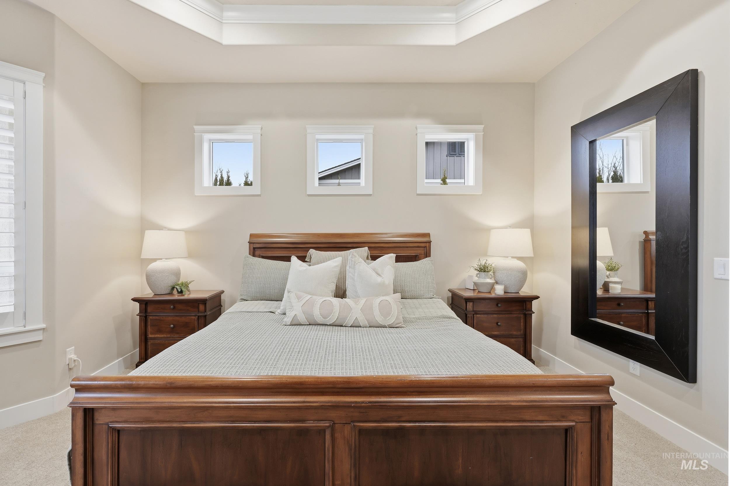 Bedroom with light carpet, multiple windows, a tray ceiling, and crown molding
