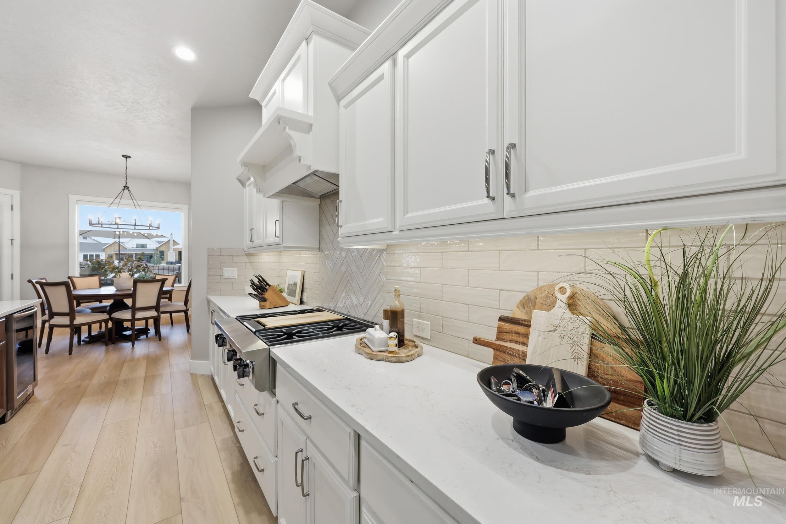 Kitchen featuring decorative light fixtures, light wood-type flooring, light stone countertops, white cabinets, and recessed lighting
