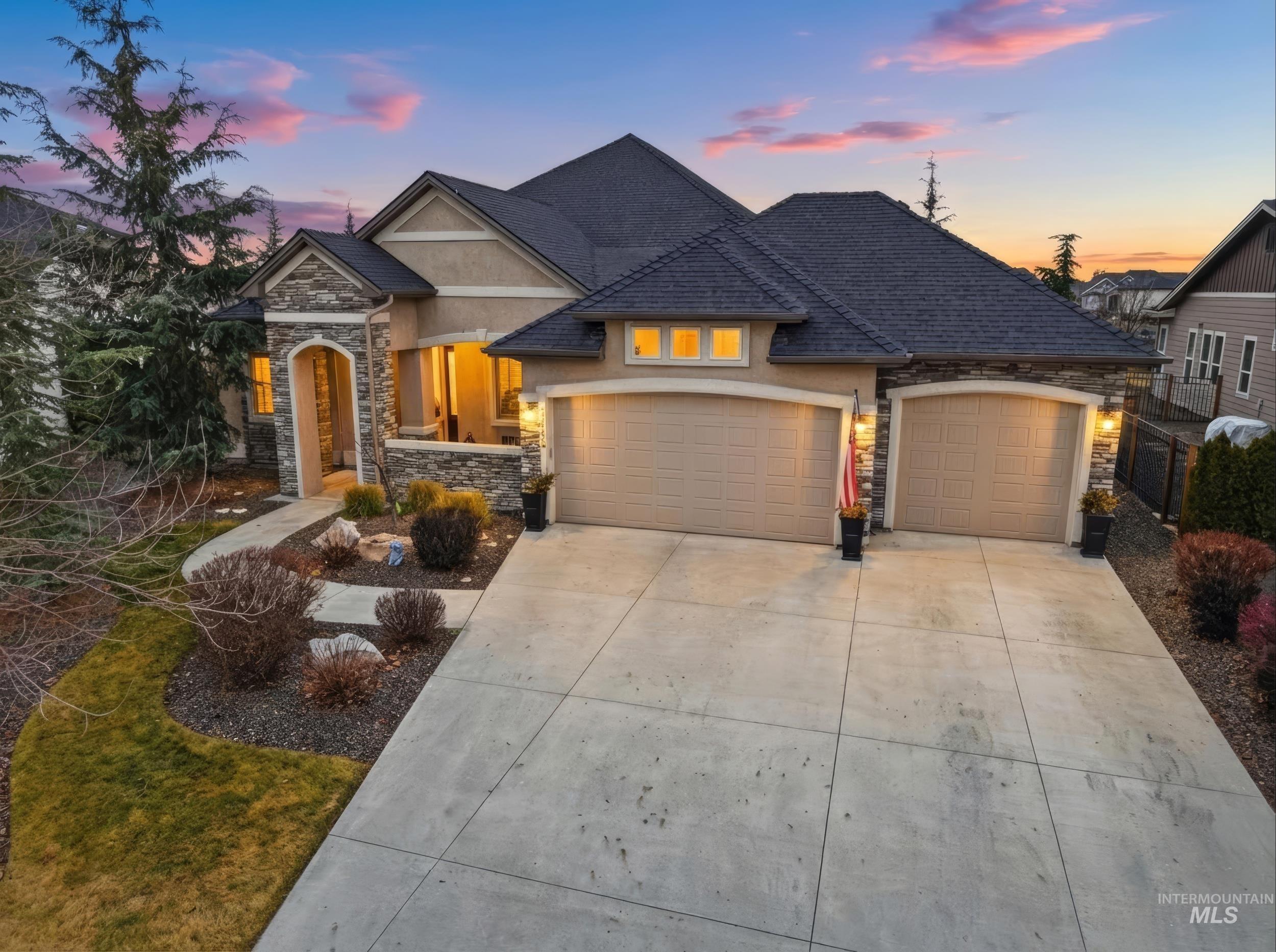 View of front facade with stone siding, stucco siding, an attached garage, and driveway