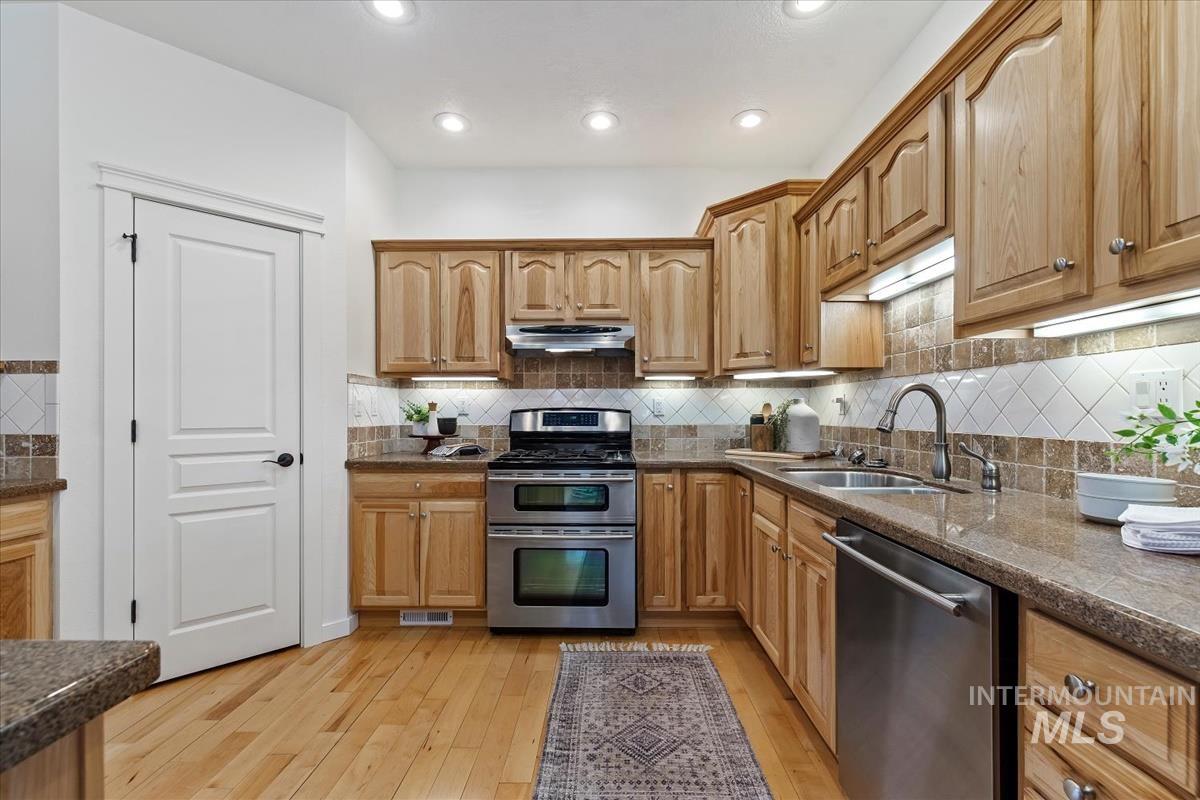 Kitchen with appliances with stainless steel finishes, light wood-type flooring, decorative backsplash, recessed lighting, and under cabinet range hood