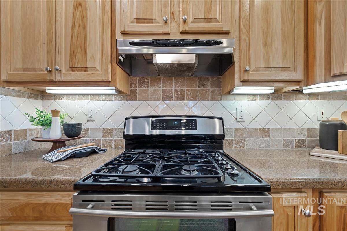 Kitchen with stainless steel gas stove, ventilation hood, tasteful backsplash, light brown cabinets, and light countertops