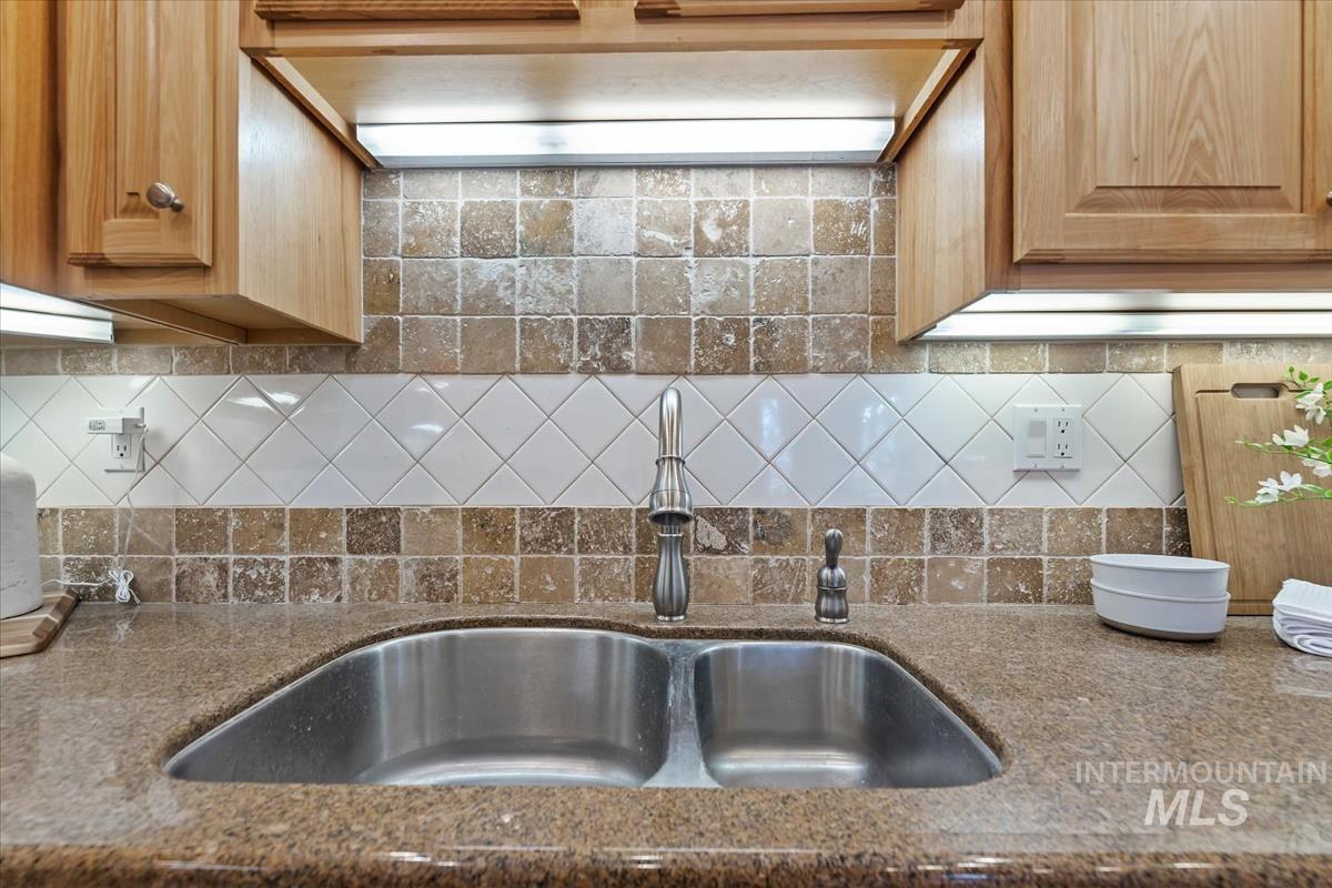 Kitchen view of custom range hood, dark stone counters, and backsplash