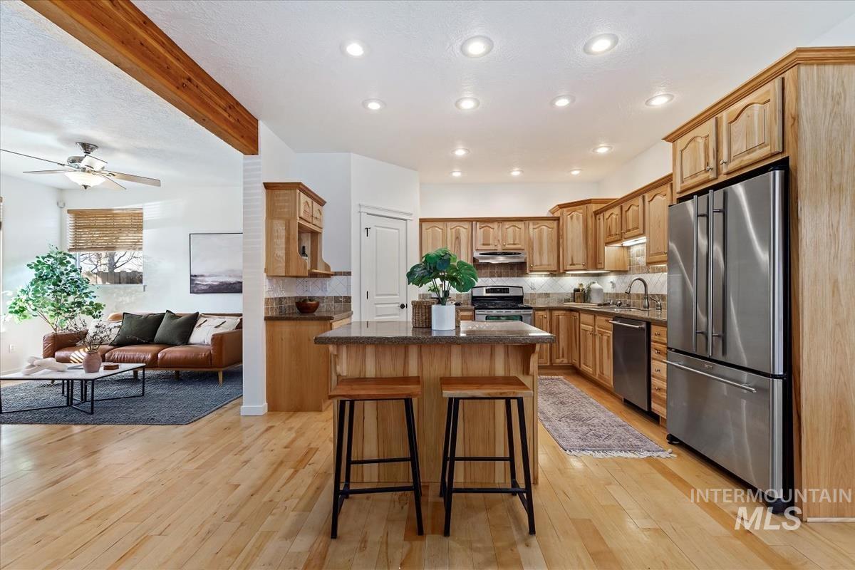 Kitchen with appliances with stainless steel finishes, open floor plan, a center island, decorative backsplash, and beamed ceiling