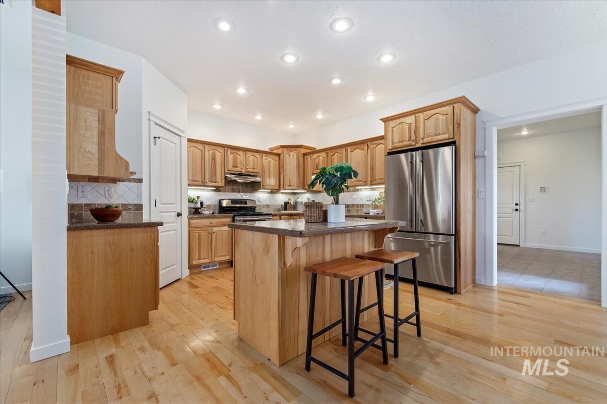 Kitchen featuring appliances with stainless steel finishes, a kitchen bar, a center island, light wood-style flooring, and backsplash
