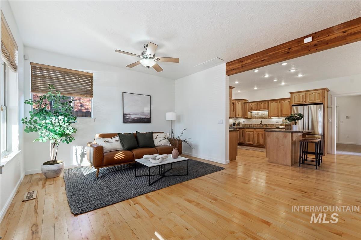 Living room featuring light wood-style floors, a ceiling fan, beam ceiling, and a textured ceiling