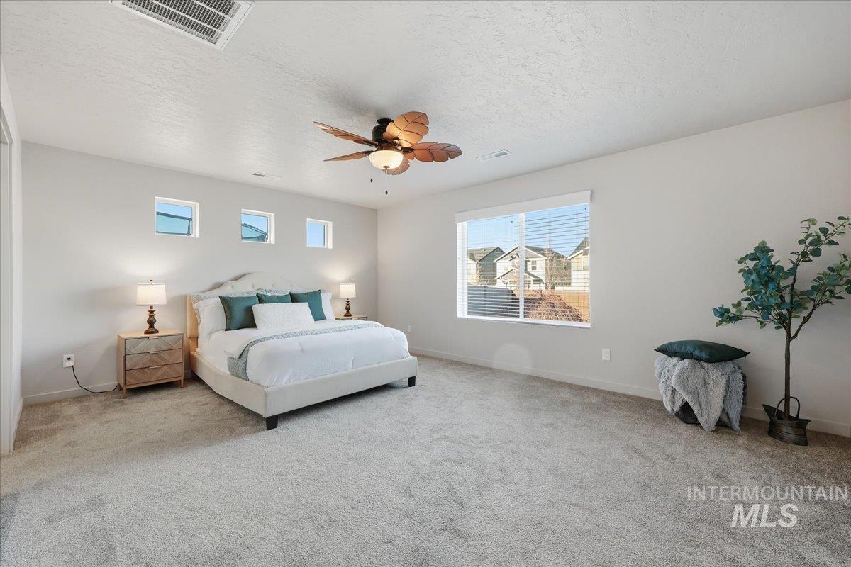 Bedroom featuring a textured ceiling, carpet, multiple windows, and ceiling fan