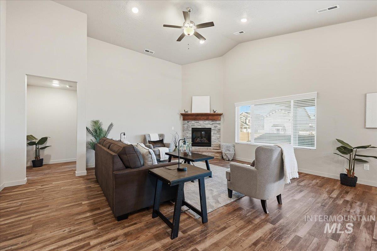 Living area with high vaulted ceiling, a stone fireplace, ceiling fan, wood finished floors, and recessed lighting