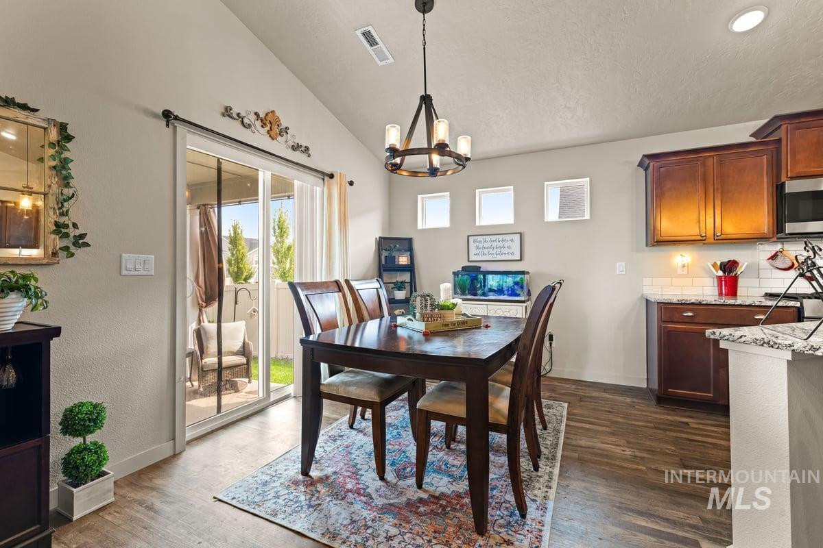 Dining space featuring vaulted ceiling, dark wood-style flooring, a chandelier, and a textured ceiling