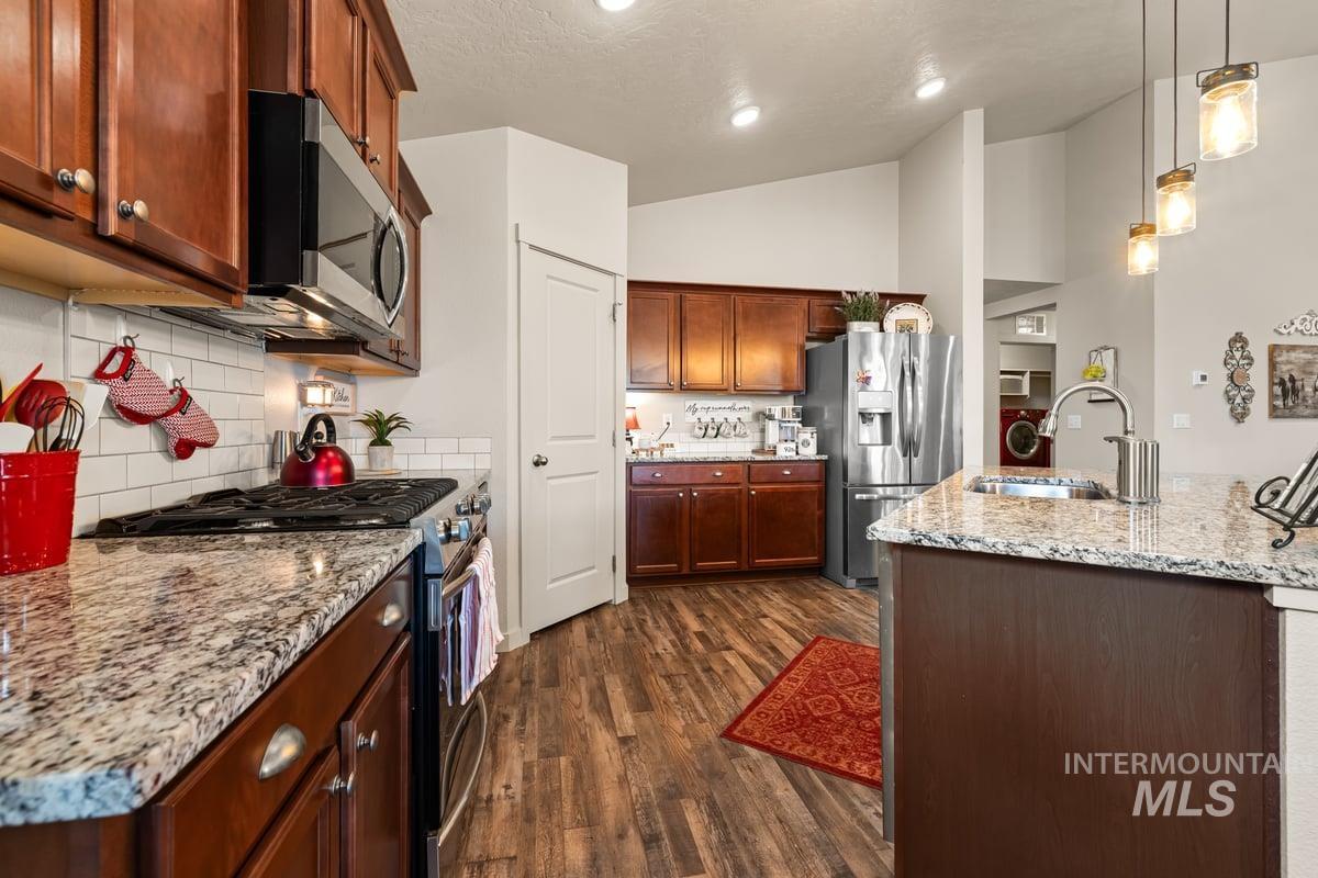 Kitchen with appliances with stainless steel finishes, light stone counters, decorative light fixtures, dark wood-style flooring, and tasteful backsplash