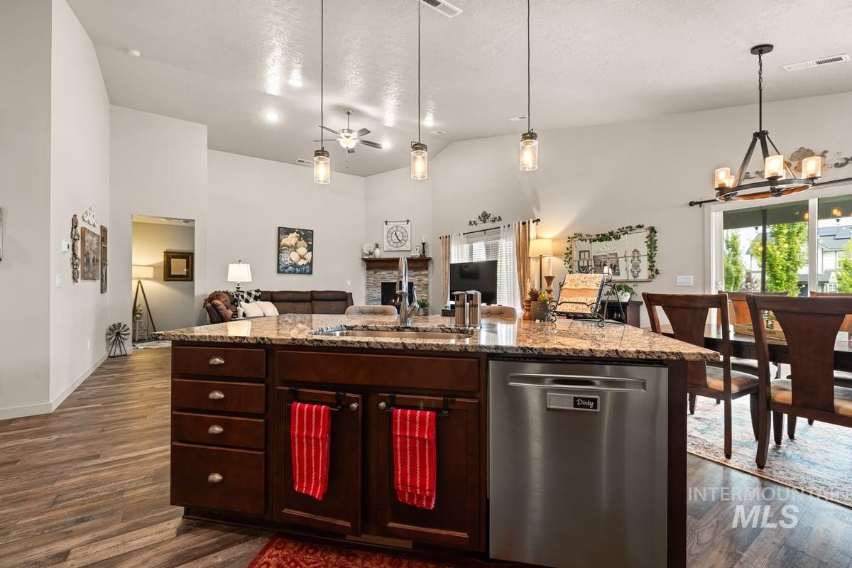 Kitchen with dishwasher, a chandelier, a fireplace, a center island with sink, and decorative light fixtures