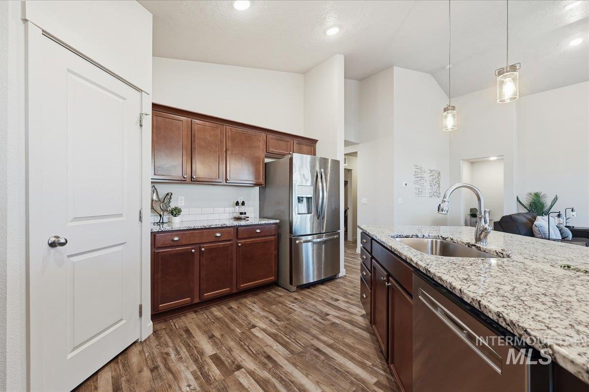 Kitchen with stainless steel appliances, light stone counters, dark wood-style flooring, pendant lighting, and high vaulted ceiling