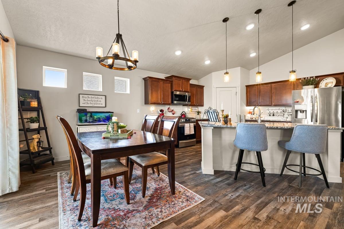 Dining area featuring dark wood-style floors, a chandelier, vaulted ceiling, and recessed lighting