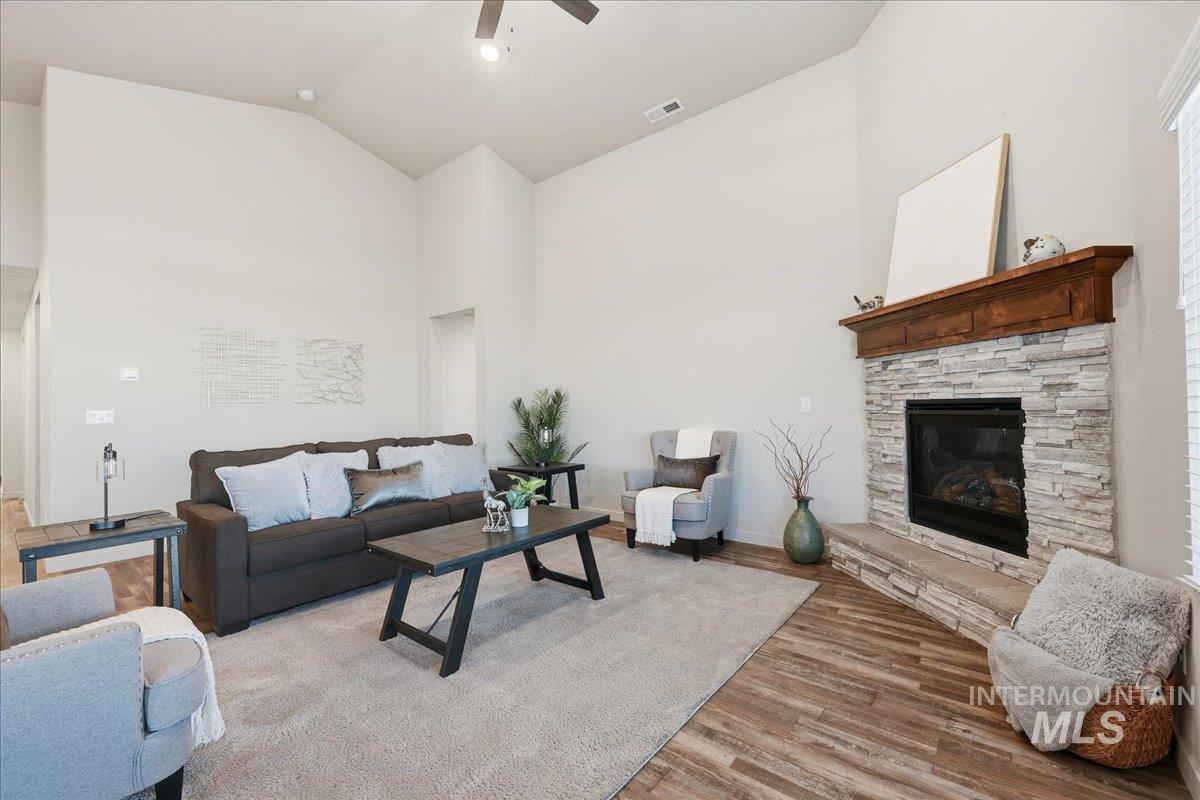 Living room featuring light wood-style floors, high vaulted ceiling, a stone fireplace, and a ceiling fan
