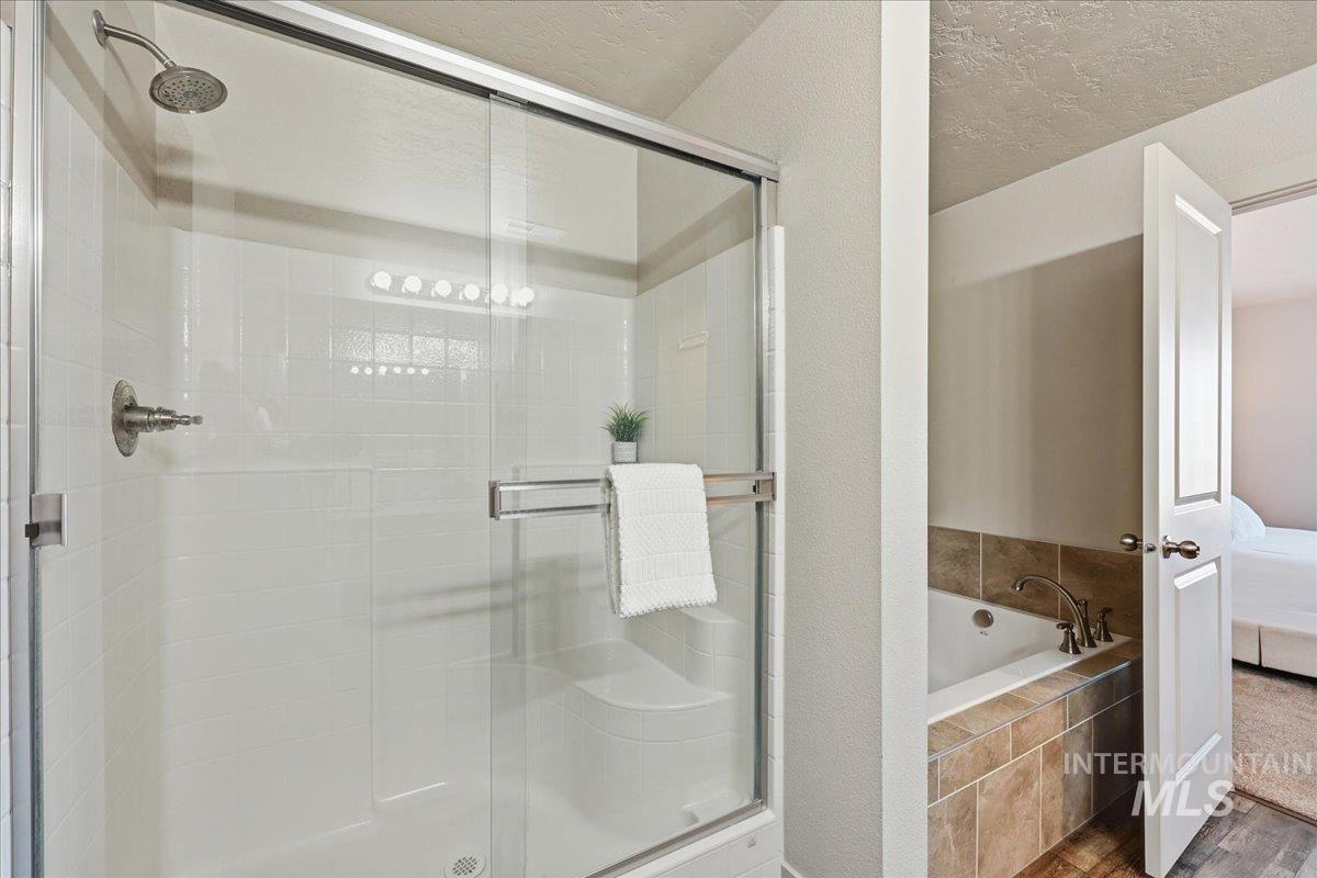 Full bathroom with connected bathroom, a stall shower, a garden tub, wood finished floors, and a textured ceiling