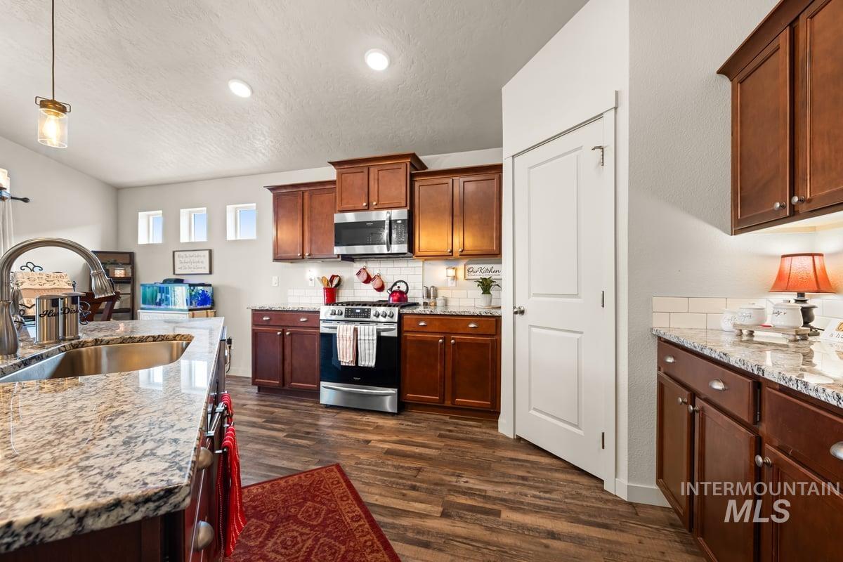 Kitchen with light stone countertops, appliances with stainless steel finishes, hanging light fixtures, dark wood finished floors, and a textured ceiling