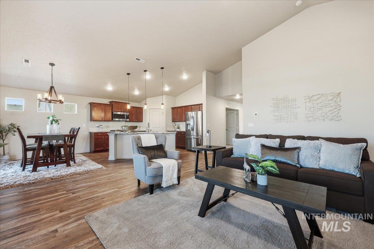 Living room with a chandelier, light wood-type flooring, and high vaulted ceiling