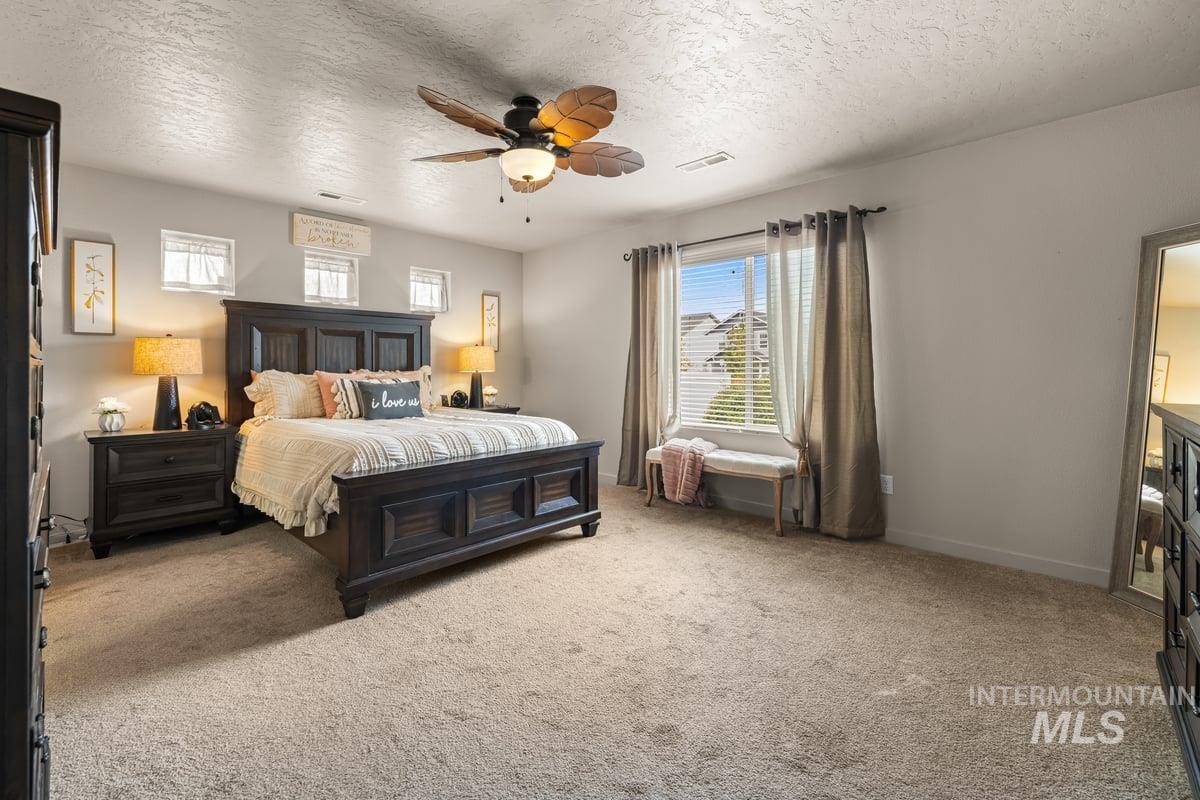 Bedroom with a textured ceiling, light colored carpet, and a ceiling fan
