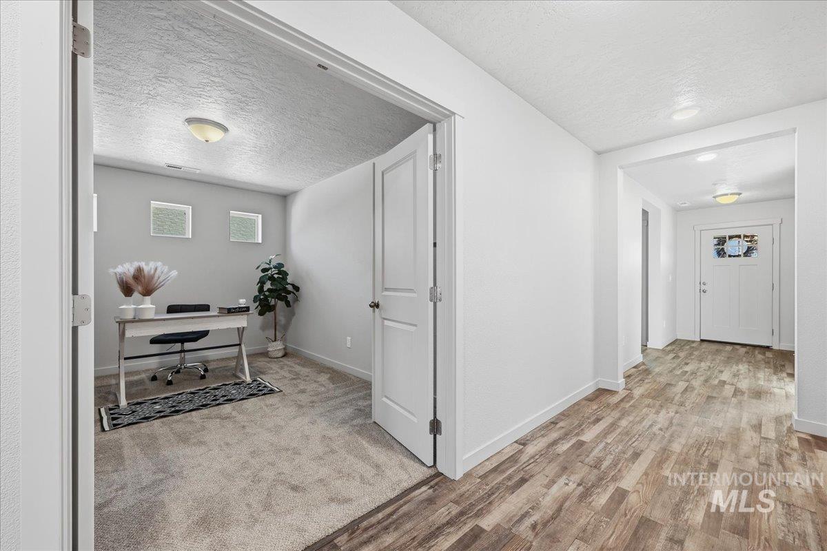 Hallway with a textured ceiling, a desk, light carpet, and light wood-style flooring