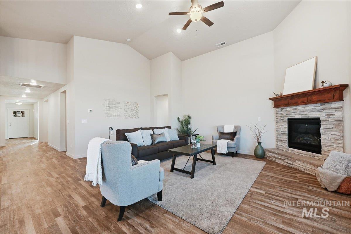Living area featuring light wood-type flooring, high vaulted ceiling, a stone fireplace, and ceiling fan