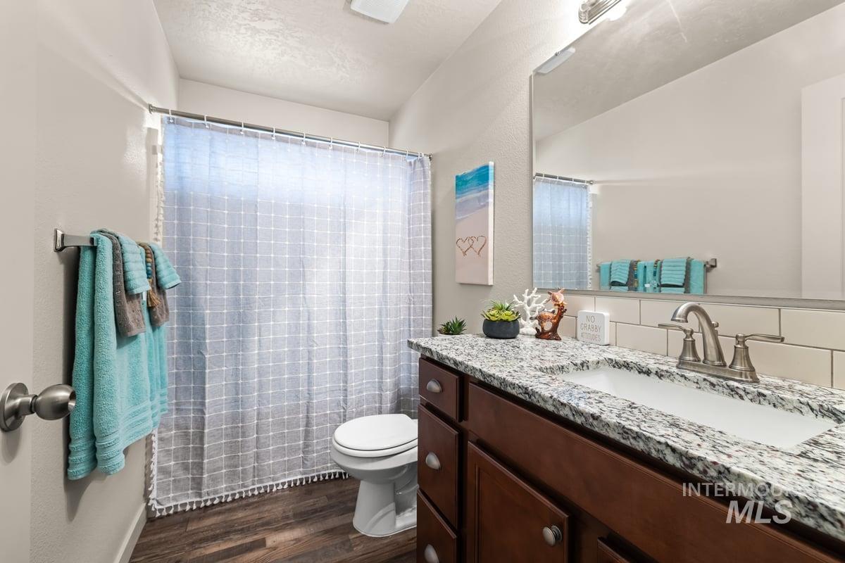 Full bathroom with vanity, dark wood finished floors, a textured ceiling, a shower with shower curtain, and a textured wall
