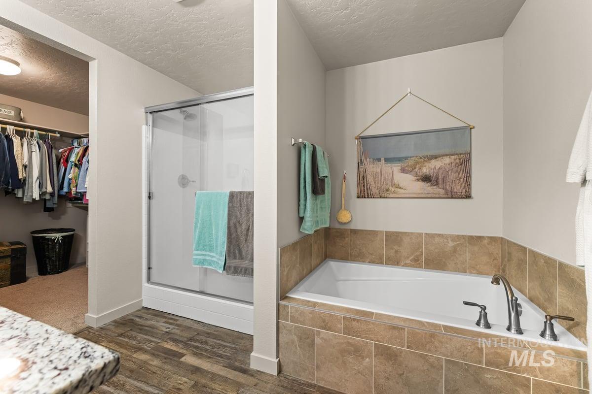 Full bathroom with a garden tub, a textured ceiling, a stall shower, a walk in closet, and dark wood-style floors