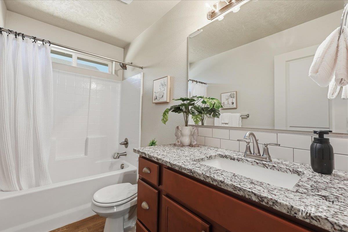 Full bath with shower / tub combo, vanity, backsplash, a textured wall, and a textured ceiling