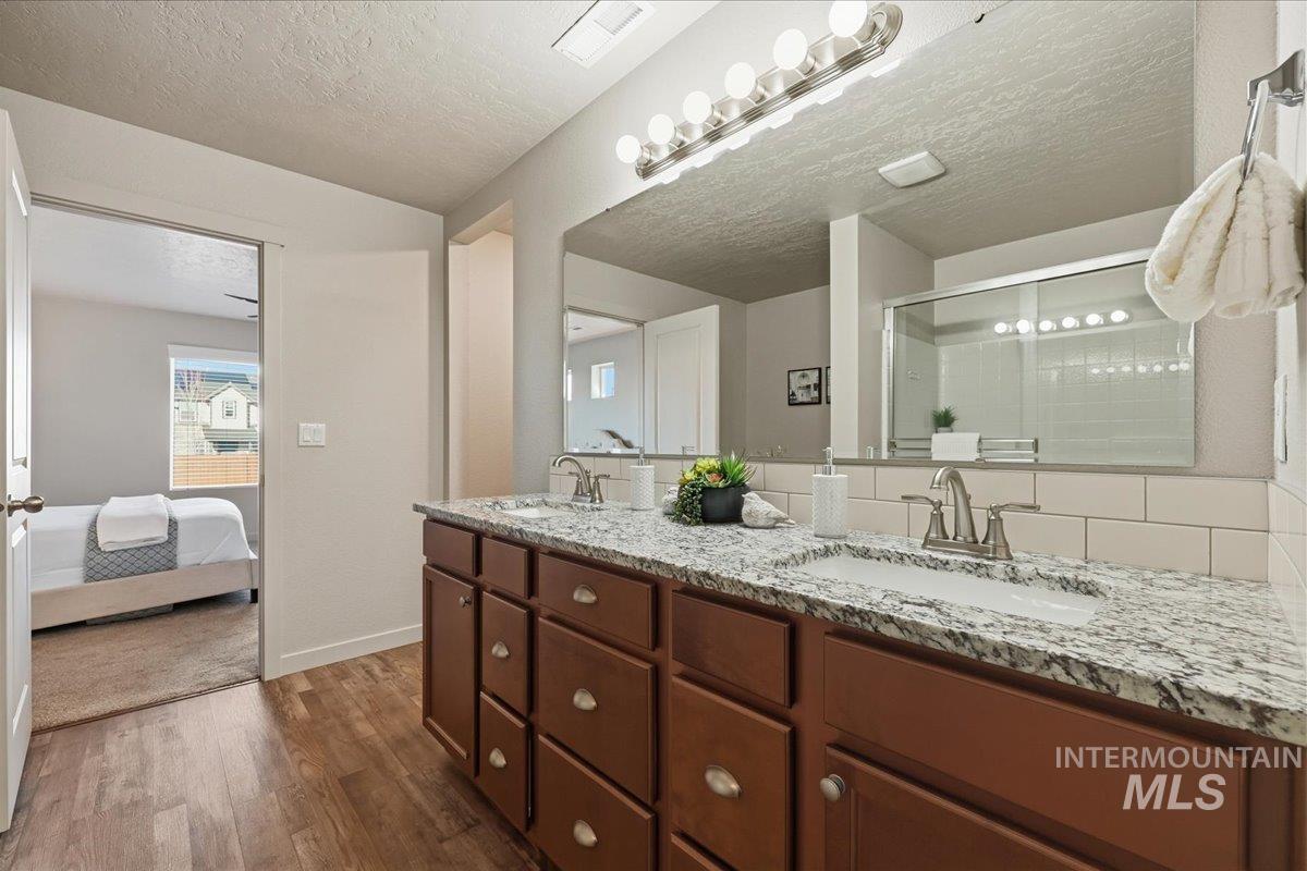 Full bath featuring double vanity, a shower stall, a textured ceiling, dark wood-style flooring, and ensuite bath