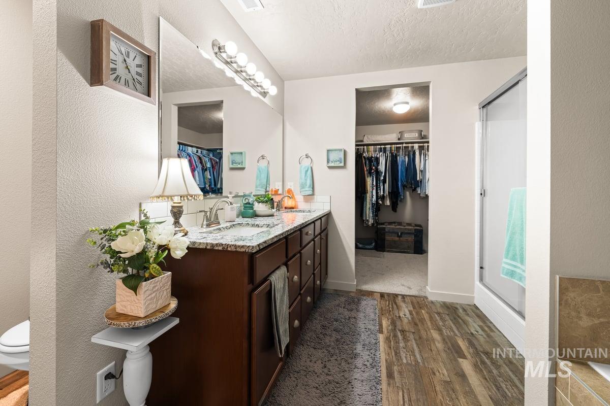 Bathroom with a spacious closet, a textured ceiling, double vanity, dark wood-type flooring, and a stall shower