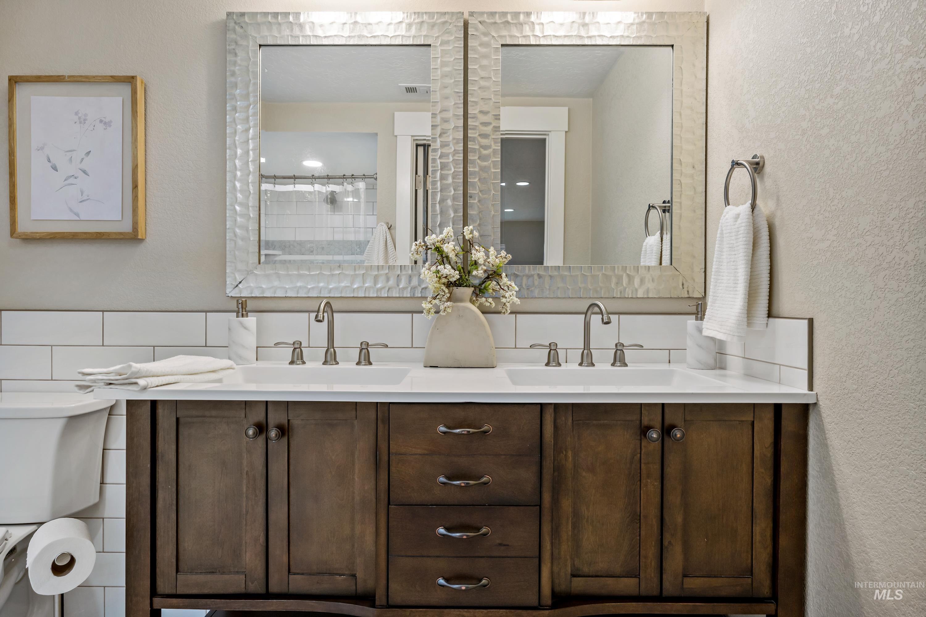 Full bathroom with a textured wall, double vanity, and a tile shower