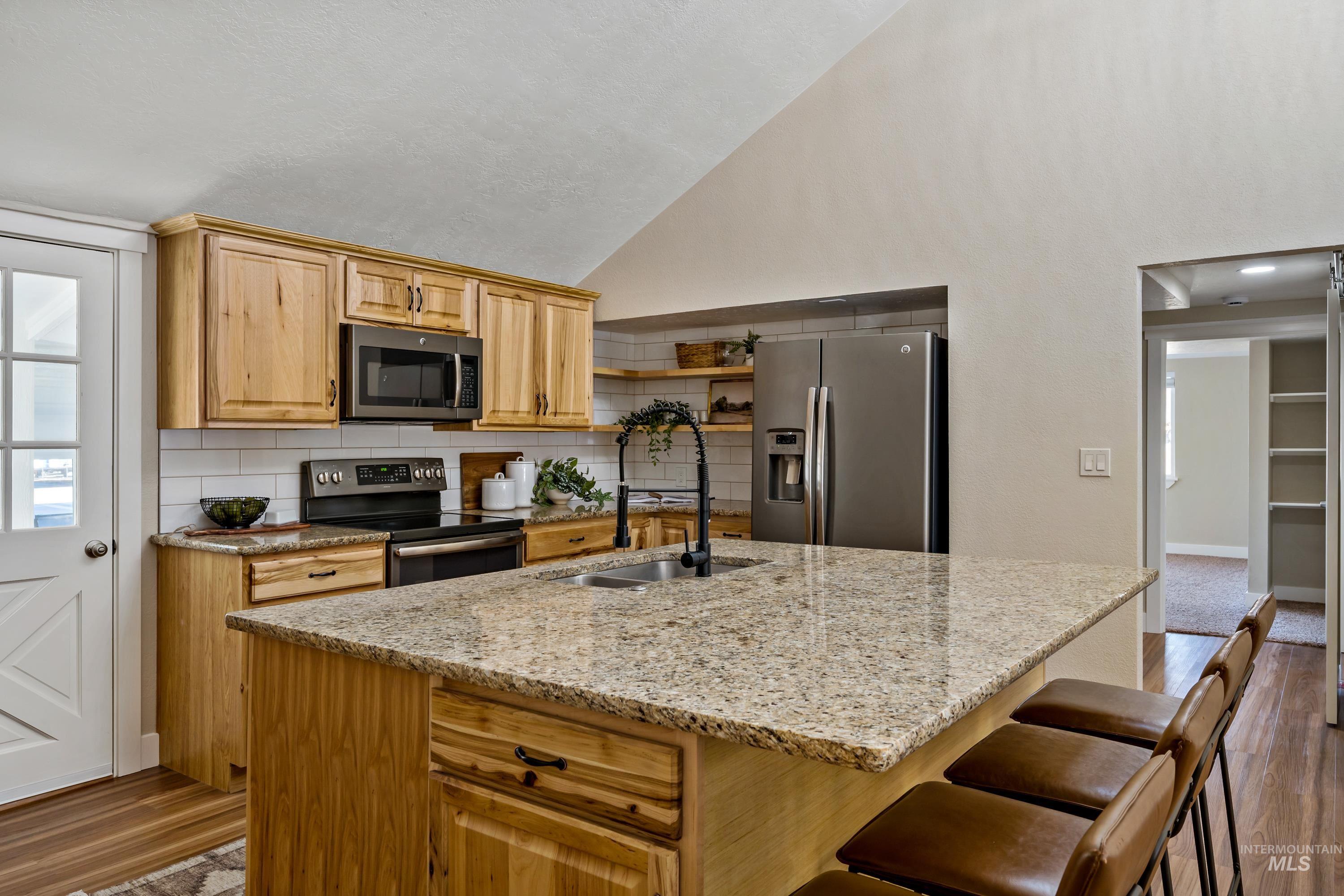 Kitchen with dark wood-style floors, stainless steel appliances, light stone countertops, backsplash, and high vaulted ceiling