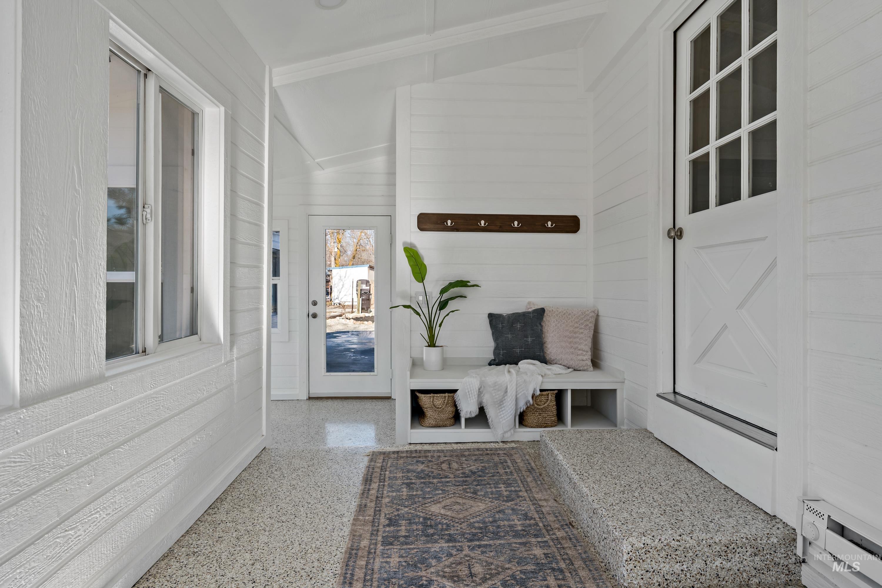 Mudroom featuring speckled floor, wooden walls, a baseboard radiator, and lofted ceiling