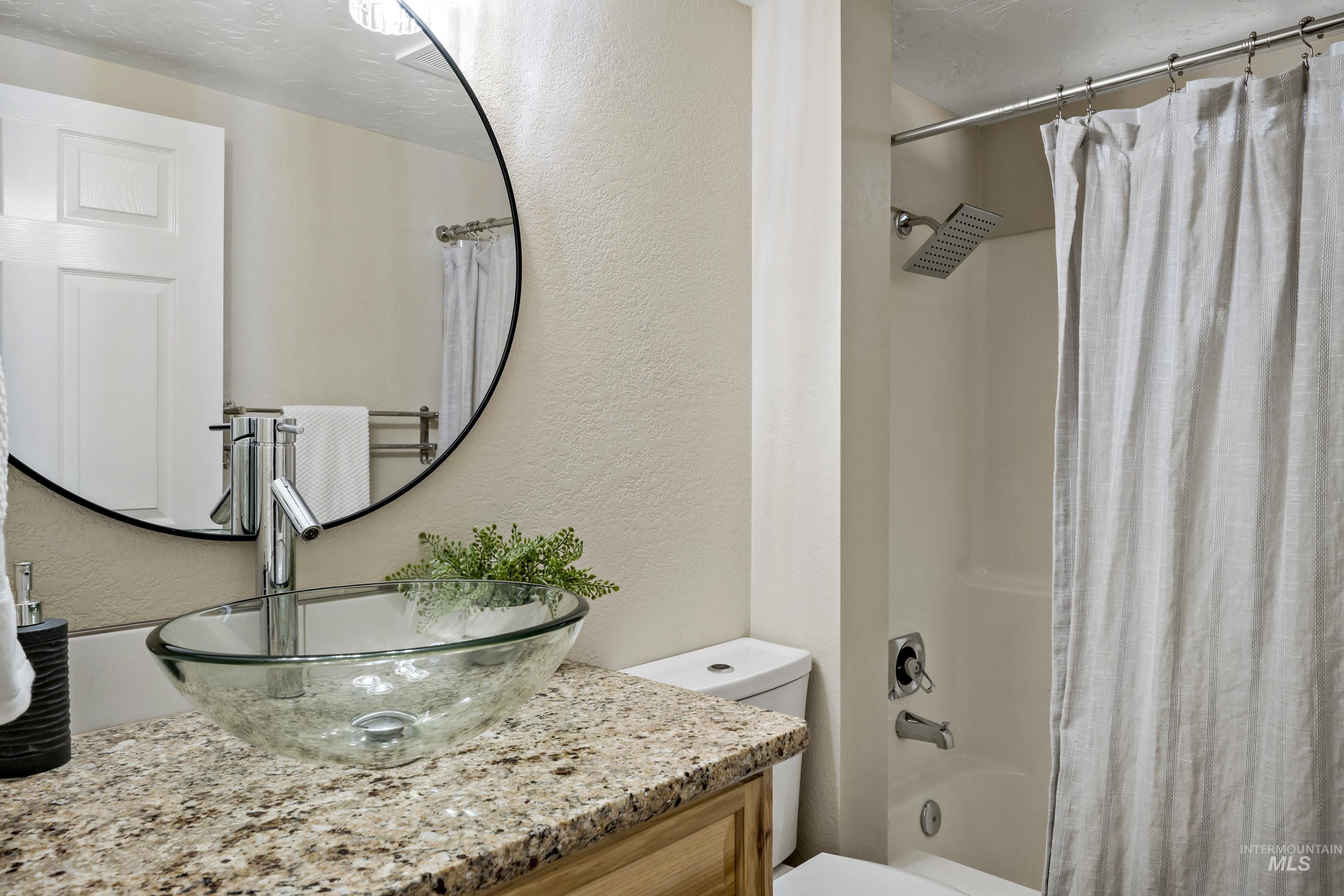 Full bathroom with a textured wall, shower / tub combo with curtain, and vanity