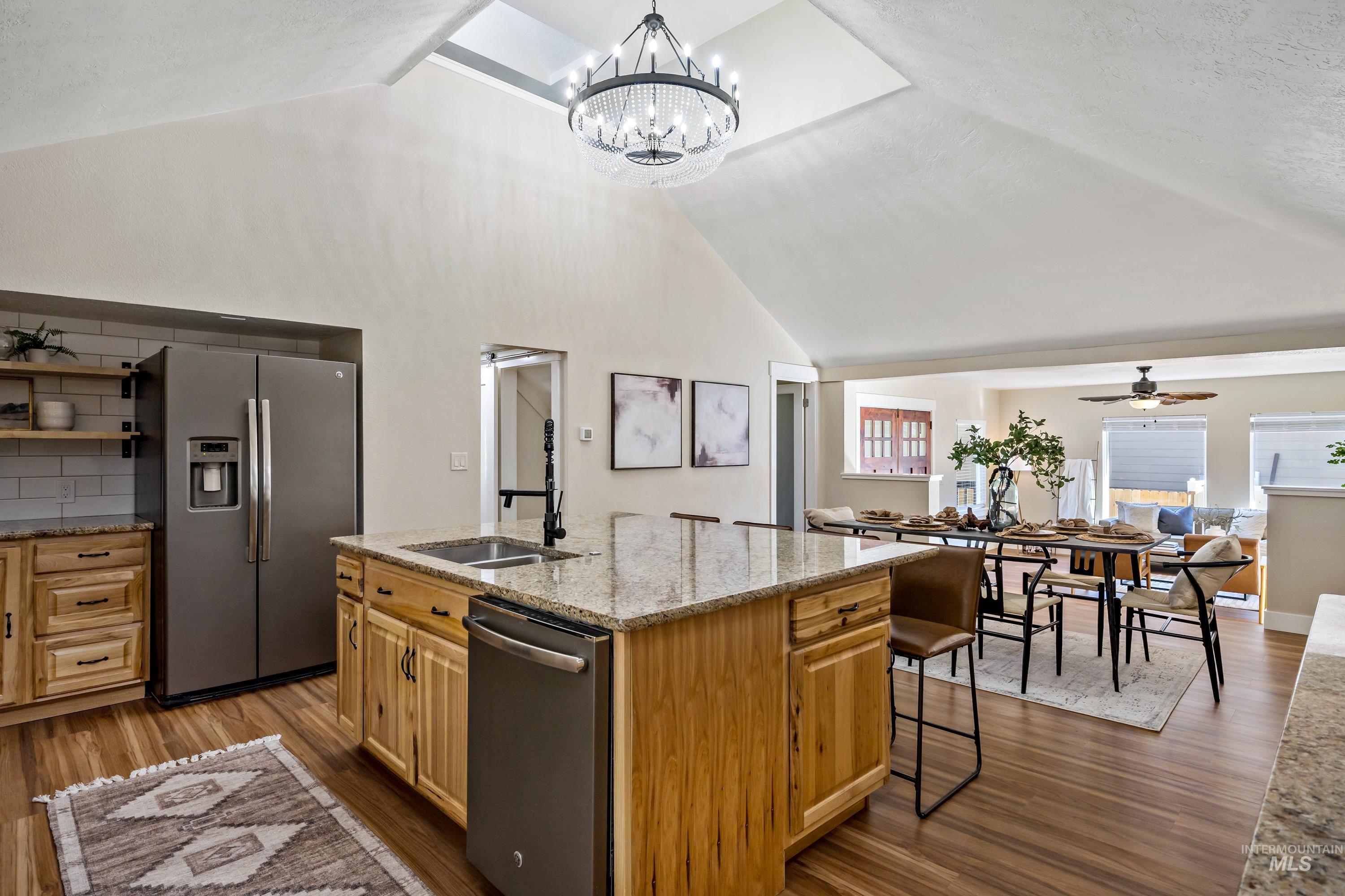 Kitchen featuring light stone counters, stainless steel appliances, dark wood-type flooring, an island with sink, and decorative light fixtures