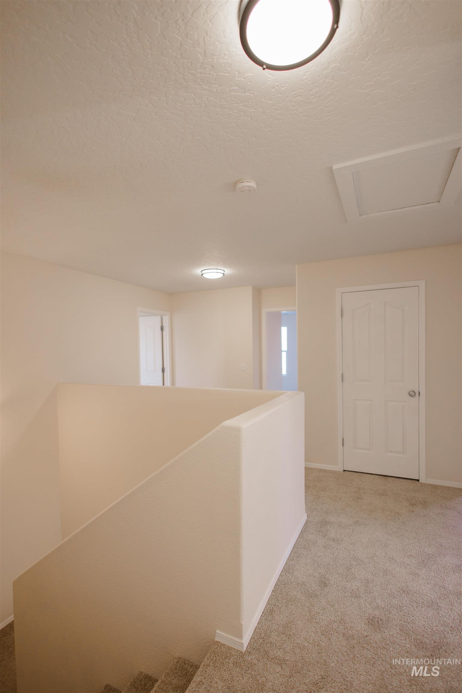 Corridor with light carpet, a textured ceiling, and attic access